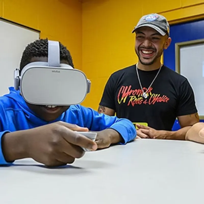 Dr. Danny Pimentel: laughing beside a young visitor trying a VR headset at a classroom table